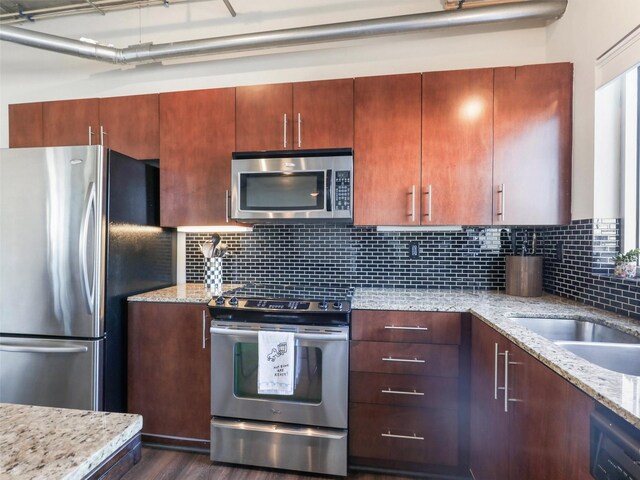 kitchen featuring appliances with stainless steel finishes, pendant lighting, sink, backsplash, and light stone counters