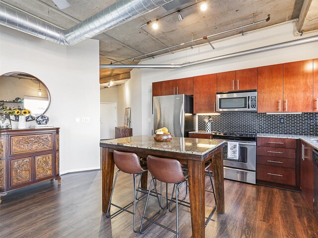 kitchen with dark wood-type flooring, stainless steel appliances, light stone countertops, and backsplash