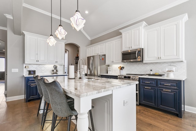 kitchen with blue cabinets, vaulted ceiling, an island with sink, stainless steel appliances, and white cabinets