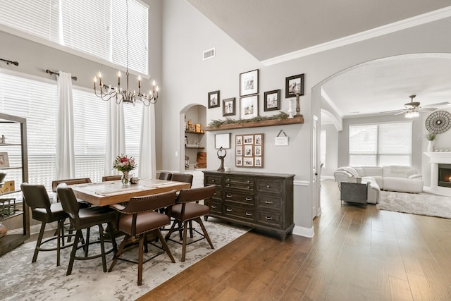 dining space with crown molding, hardwood / wood-style flooring, ceiling fan with notable chandelier, and a high ceiling