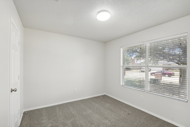 spare room with a textured ceiling and dark colored carpet