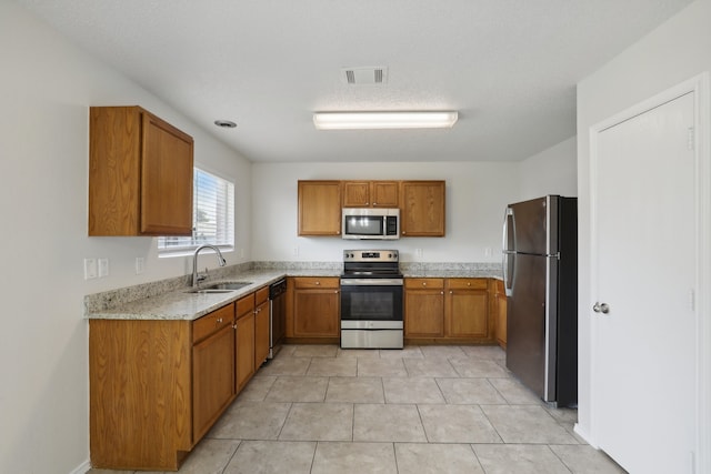 kitchen featuring light stone counters, a textured ceiling, stainless steel appliances, sink, and light tile patterned flooring