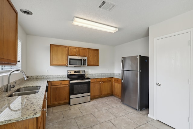 kitchen with sink, light tile patterned floors, a textured ceiling, appliances with stainless steel finishes, and light stone counters