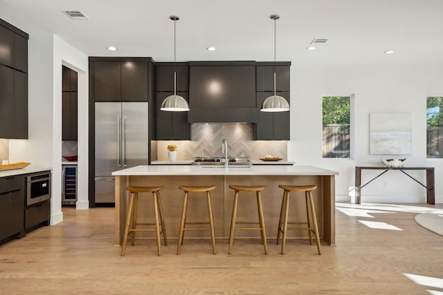 kitchen with a center island with sink, decorative backsplash, decorative light fixtures, a kitchen bar, and stainless steel built in refrigerator