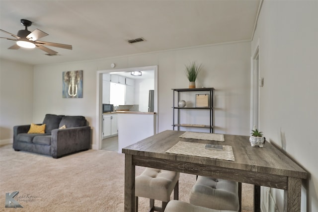 carpeted dining room with ceiling fan and crown molding