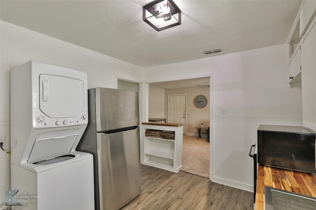 laundry room featuring a textured ceiling, light hardwood / wood-style floors, and stacked washer and clothes dryer