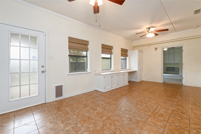 unfurnished living room featuring ceiling fan, light tile patterned flooring, ornamental molding, and brick wall