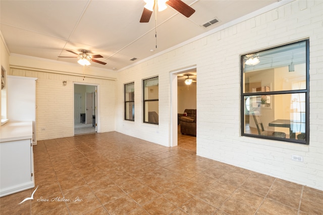 unfurnished room featuring ceiling fan, crown molding, and brick wall