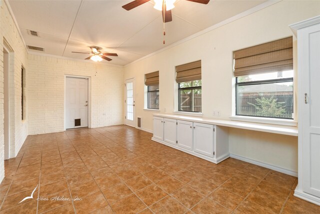 tiled empty room with ceiling fan, crown molding, and brick wall