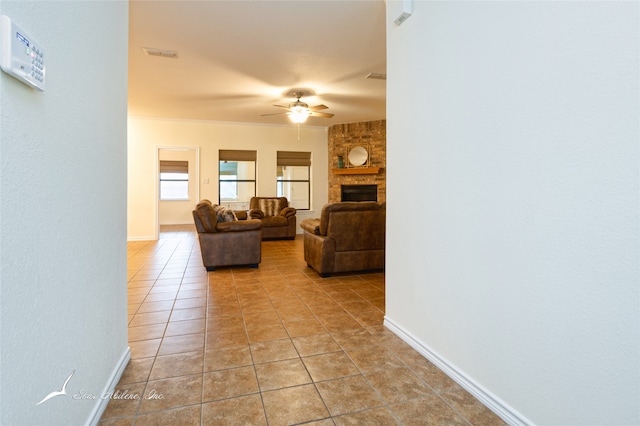 living room featuring light tile patterned floors, a stone fireplace, ceiling fan, and ornamental molding