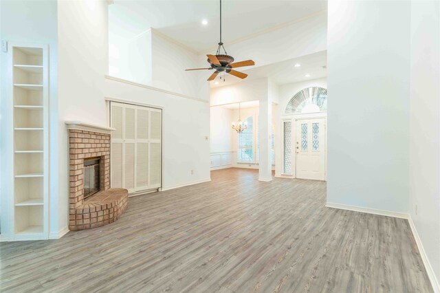 unfurnished living room featuring a towering ceiling, light wood-type flooring, built in shelves, ceiling fan with notable chandelier, and a fireplace