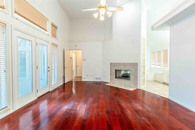 unfurnished living room featuring a towering ceiling, built in shelves, ceiling fan, a fireplace, and hardwood / wood-style floors