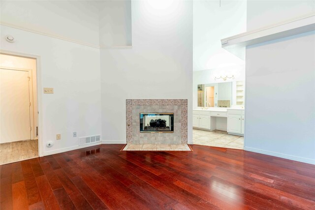 unfurnished living room featuring a high ceiling, light wood-type flooring, and a tiled fireplace