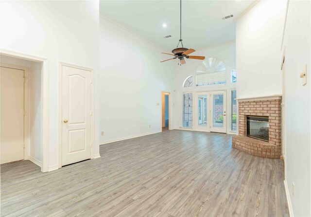 unfurnished living room featuring a high ceiling, a brick fireplace, ceiling fan, light wood-type flooring, and ornamental molding