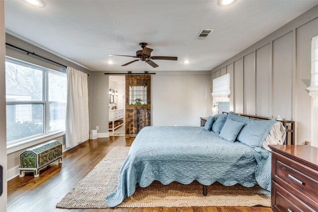 bedroom featuring hardwood / wood-style floors, ceiling fan, and a barn door