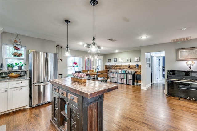 kitchen featuring white cabinetry, hanging light fixtures, light stone counters, stainless steel fridge, and a kitchen island