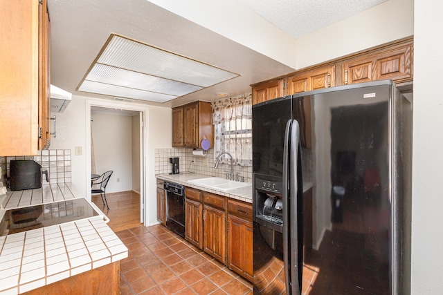 kitchen featuring backsplash, ventilation hood, sink, black appliances, and tile countertops