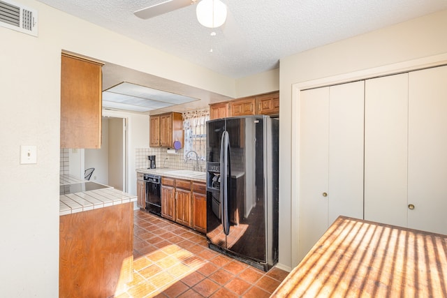 kitchen featuring ceiling fan, tile counters, sink, tasteful backsplash, and black appliances