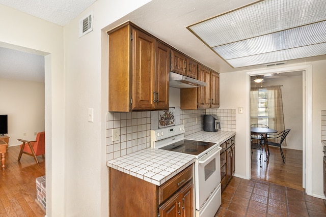 kitchen with tile countertops, stove, backsplash, dark wood-type flooring, and a textured ceiling