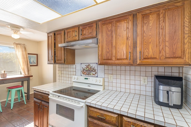 kitchen featuring ceiling fan, tile counters, dark tile patterned floors, backsplash, and range