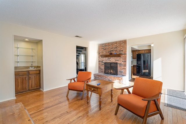 living room with a fireplace, sink, light hardwood / wood-style floors, and a textured ceiling