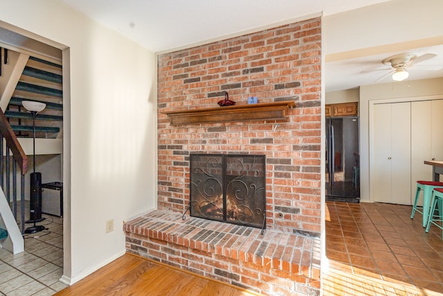 living room with a brick fireplace, light hardwood / wood-style flooring, and ceiling fan