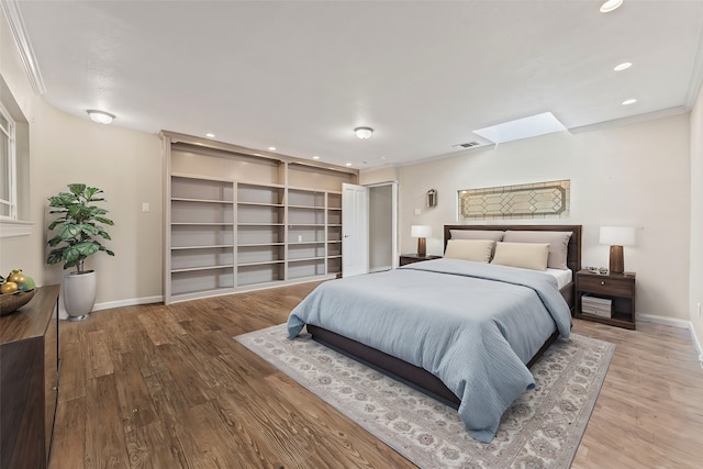 bedroom featuring a skylight, crown molding, and light hardwood / wood-style flooring