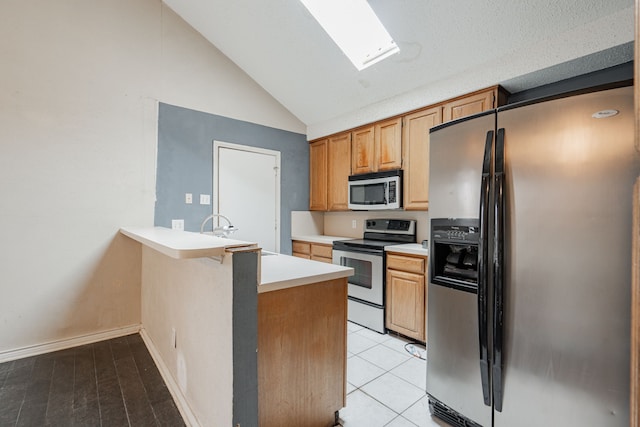 kitchen featuring sink, light hardwood / wood-style flooring, vaulted ceiling with skylight, appliances with stainless steel finishes, and kitchen peninsula