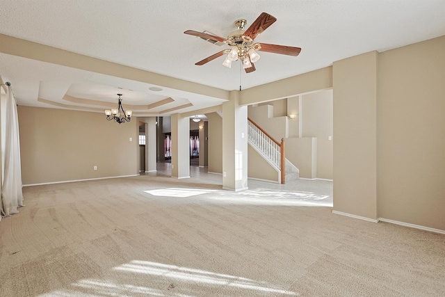 unfurnished living room with a raised ceiling, light colored carpet, and ceiling fan with notable chandelier