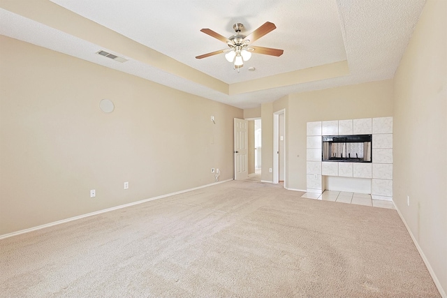 unfurnished living room with a raised ceiling, ceiling fan, a textured ceiling, light colored carpet, and a tiled fireplace