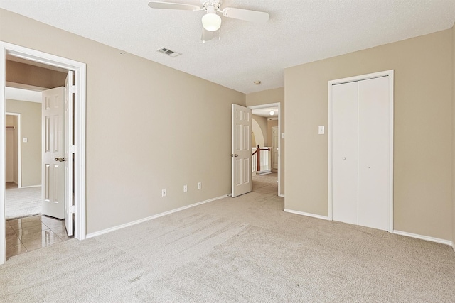 unfurnished bedroom featuring ceiling fan, light colored carpet, a textured ceiling, and a closet