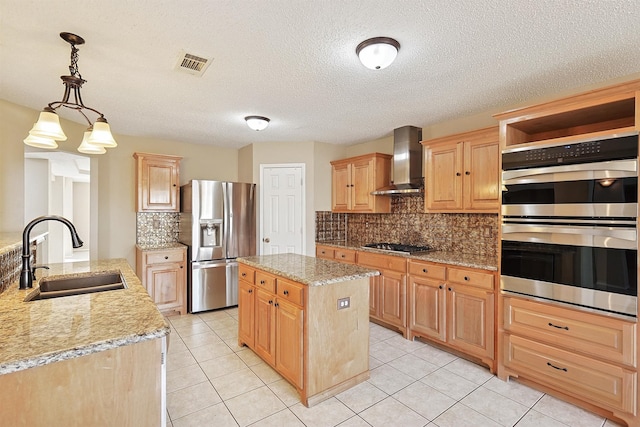 kitchen with sink, wall chimney exhaust hood, decorative light fixtures, a kitchen island, and stainless steel appliances