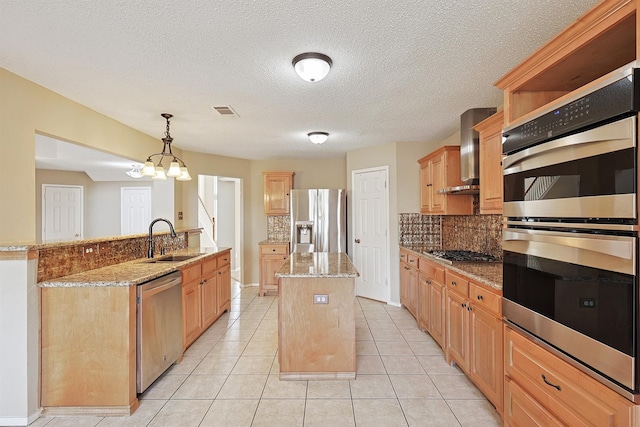 kitchen with a center island, sink, stainless steel appliances, wall chimney range hood, and decorative light fixtures