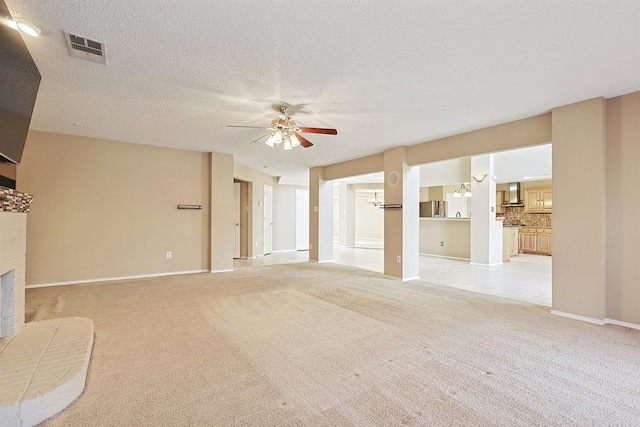 unfurnished living room featuring ceiling fan, a fireplace, light colored carpet, and a textured ceiling