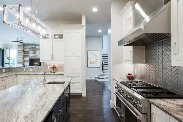 kitchen with white cabinets, high end stainless steel range oven, hanging light fixtures, and wall chimney range hood