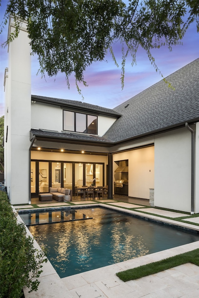 back house at dusk with an outdoor living space and a patio