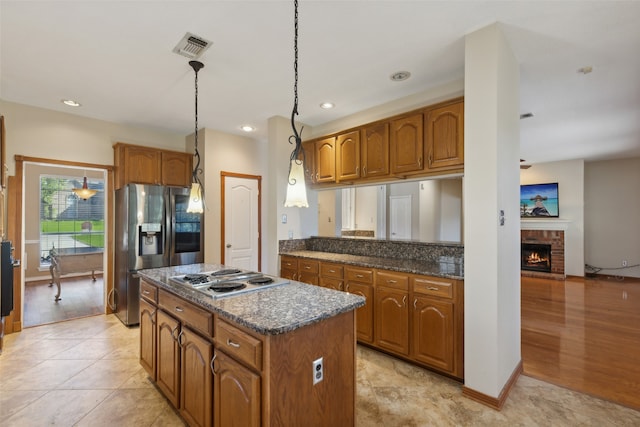 kitchen with a center island, white gas cooktop, hanging light fixtures, light hardwood / wood-style flooring, and stainless steel fridge