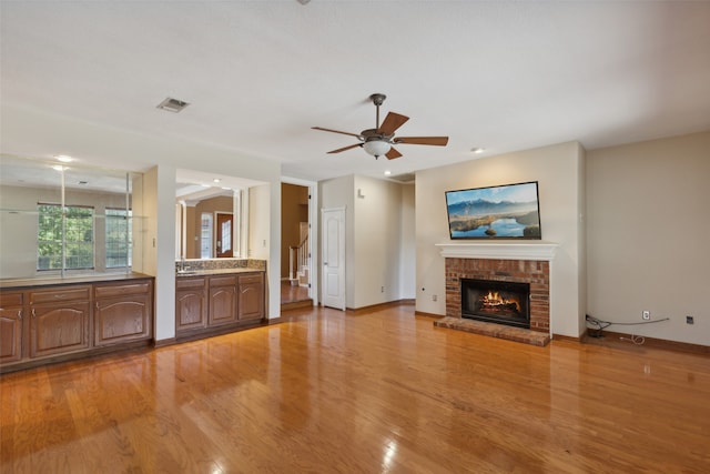 unfurnished living room featuring ceiling fan, light hardwood / wood-style floors, and a brick fireplace