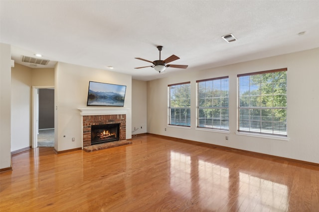 unfurnished living room featuring a brick fireplace, ceiling fan, a textured ceiling, and light hardwood / wood-style flooring