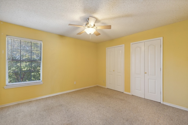 unfurnished bedroom featuring multiple closets, ceiling fan, carpet floors, and a textured ceiling