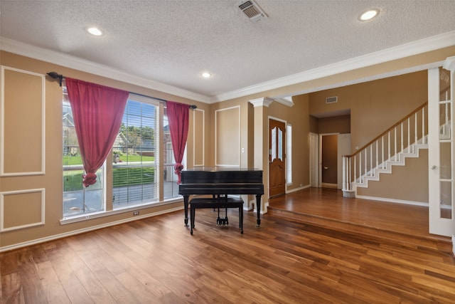 misc room featuring hardwood / wood-style floors, ornamental molding, a textured ceiling, and decorative columns