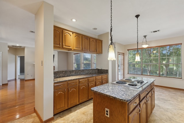 kitchen with dark stone counters, pendant lighting, stainless steel gas stovetop, a kitchen island, and light wood-type flooring