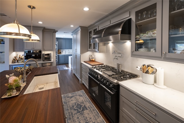 kitchen with stainless steel oven, double oven range, dark wood-type flooring, ventilation hood, and decorative light fixtures