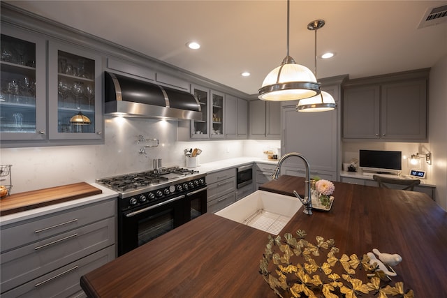 kitchen featuring pendant lighting, stainless steel microwave, high end black range, ventilation hood, and sink