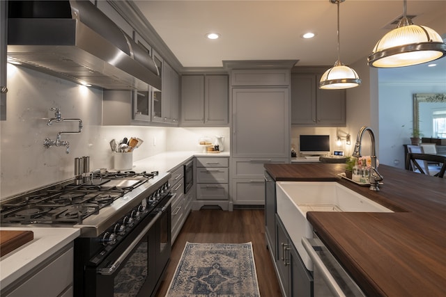 kitchen with gas stove, sink, wall chimney range hood, wood counters, and pendant lighting