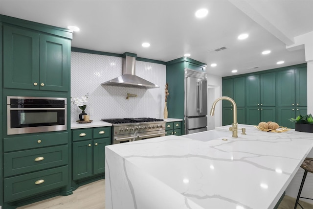 kitchen with green cabinetry, light stone countertops, wall chimney range hood, and high end appliances