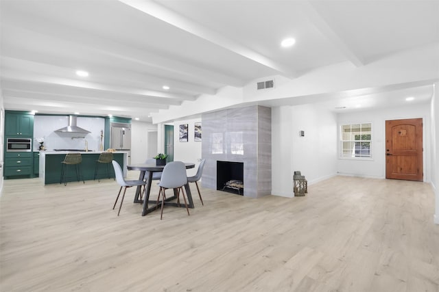 dining room featuring light hardwood / wood-style floors, beam ceiling, and a tile fireplace