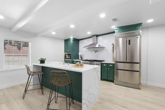 kitchen featuring appliances with stainless steel finishes, a kitchen breakfast bar, wall chimney range hood, light hardwood / wood-style flooring, and green cabinets