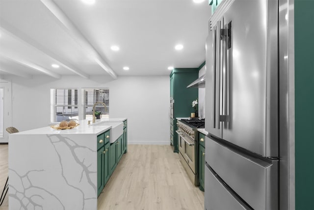 kitchen featuring light stone countertops, premium appliances, sink, green cabinetry, and light hardwood / wood-style floors