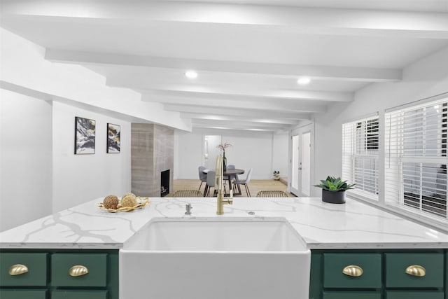 kitchen with light stone counters, sink, a tile fireplace, beamed ceiling, and green cabinets